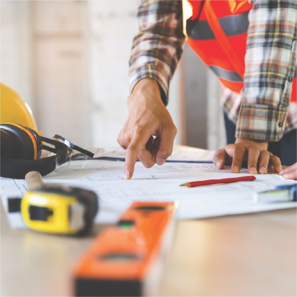 Construction worker reviewing blueprints with tools on the table.