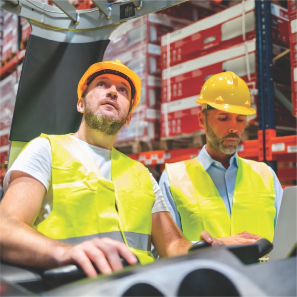 Warehouse workers in hard hats operating equipment and reviewing data.