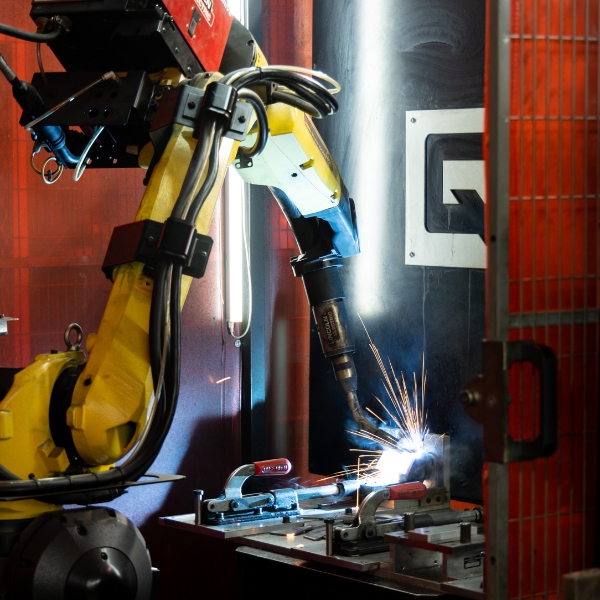 Industrial robotic arm welding metal components in a manufacturing facility