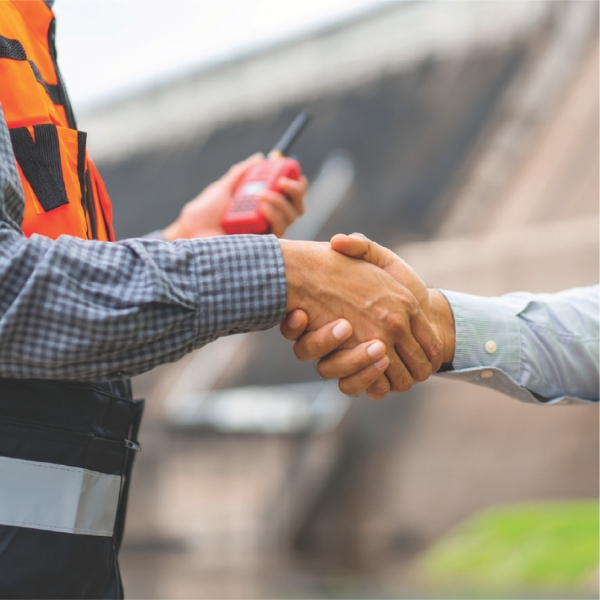Worker in safety vest shaking hands while holding a radio.