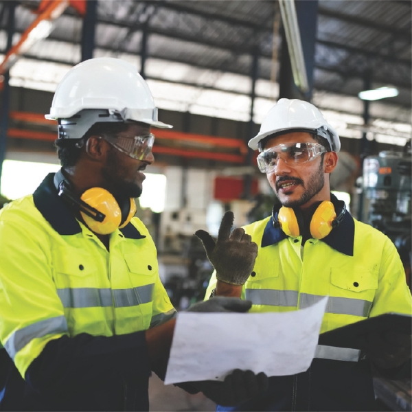 Two factory workers in safety gear reviewing a document